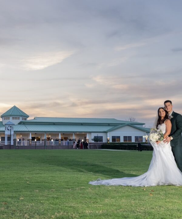A bride and groom standing with Ocoee Lakeshore Center in the background on a grass field.