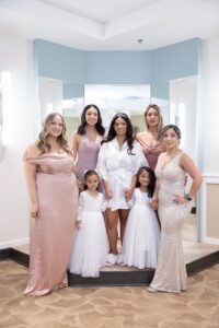 A bride in a white rob standing with her bridesmaids in mauve and blush with flower girls inside a bridal suite at Ocoee Lakeshore Center.