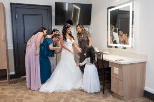 A bride putting on her white lace wedding gown with the help of bridesmaids and family inside a bridal suite at Ocoee Lakeshore Center.