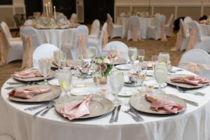 A ballroom at Ocoee Lakeshore Center ready for a white and blush pink wedding reception with circular tables set with champagne plates and blush pink napkins.