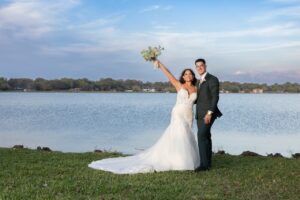A bride and groom standing next to stark lake at Ocoee Lakeshore Center holding up a bouquet.