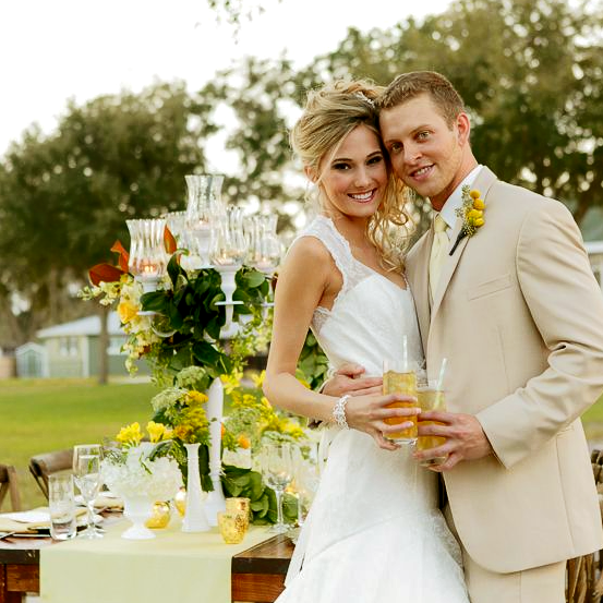 A bride and groom outside of Ocoee Lakeshore Center holding summer drinks with a yellow and green tablescape in the background.