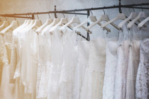 A variety of styles of white wedding dresses hanging from a rack.