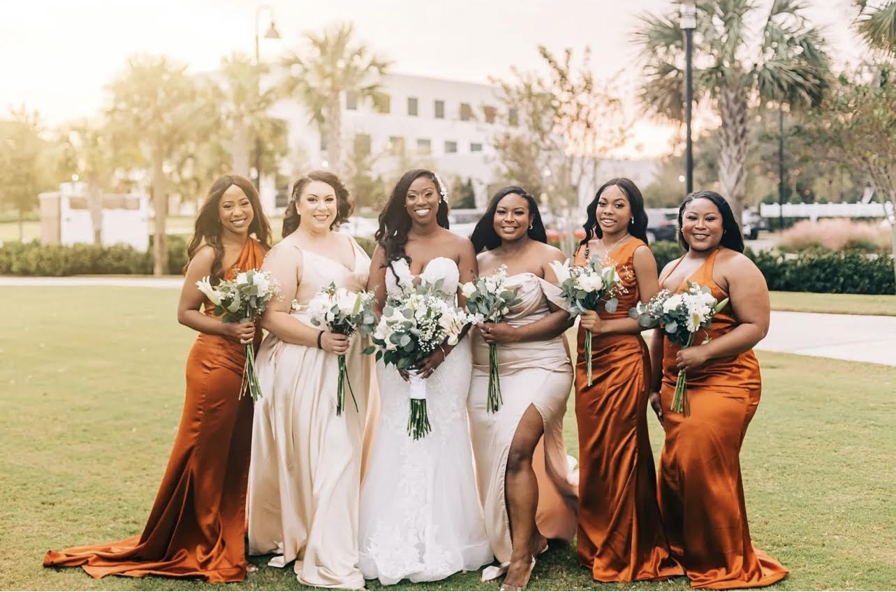 bridesmaids in rust and bride in white dress standing together side by side outside ooee lakeshore center.