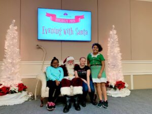 Santa and children inside Ocoee Lakeshore Center on Stage with White Christmas Trees for and Evening with Santa.