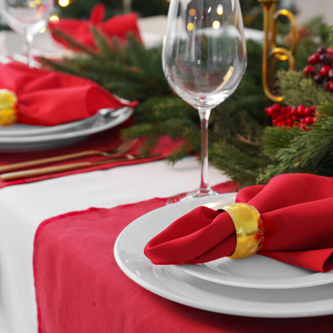 A holiday tablescape with red linen and white linen, christmas decor wine glasses.